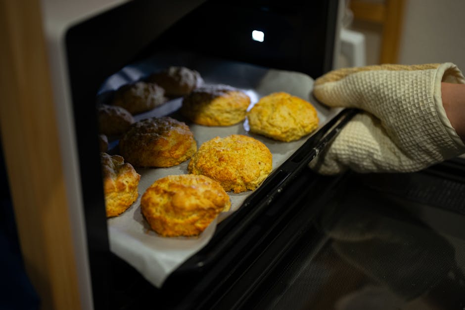 オーブンミットを使って焼きたてのビスケットをオーブンから取り出す、温かく魅力的な光景。
